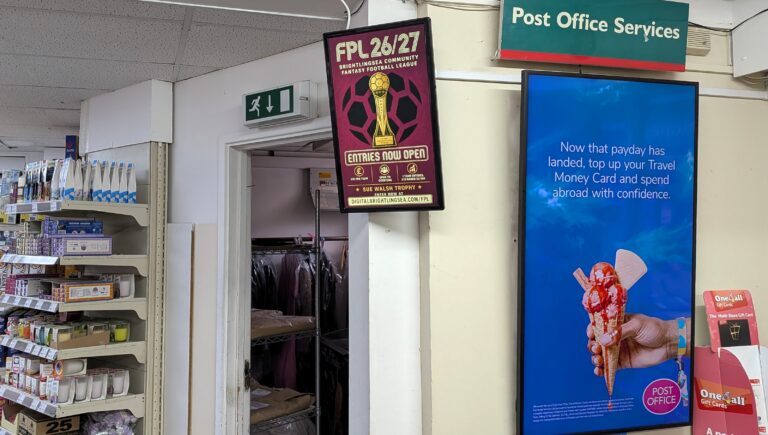 A portrait advert for the 2026/27 Brightlingsea Community Fantasy Football League displayed inside Brightlingsea Post Office, next to the larger Post Office digital screen. The advert features the Sue Walsh Community Fantasy Football Trophy and says entries are now open.